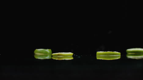 Ringe-Aus-Frischen-Grünen-Limettenscheiben-Fallen-Mit-Wasserspritzern-In-Zeitlupe-Auf-Das-Glas